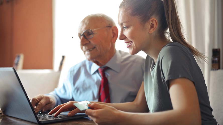 Older man and younger lady smiling and looking at a laptop
